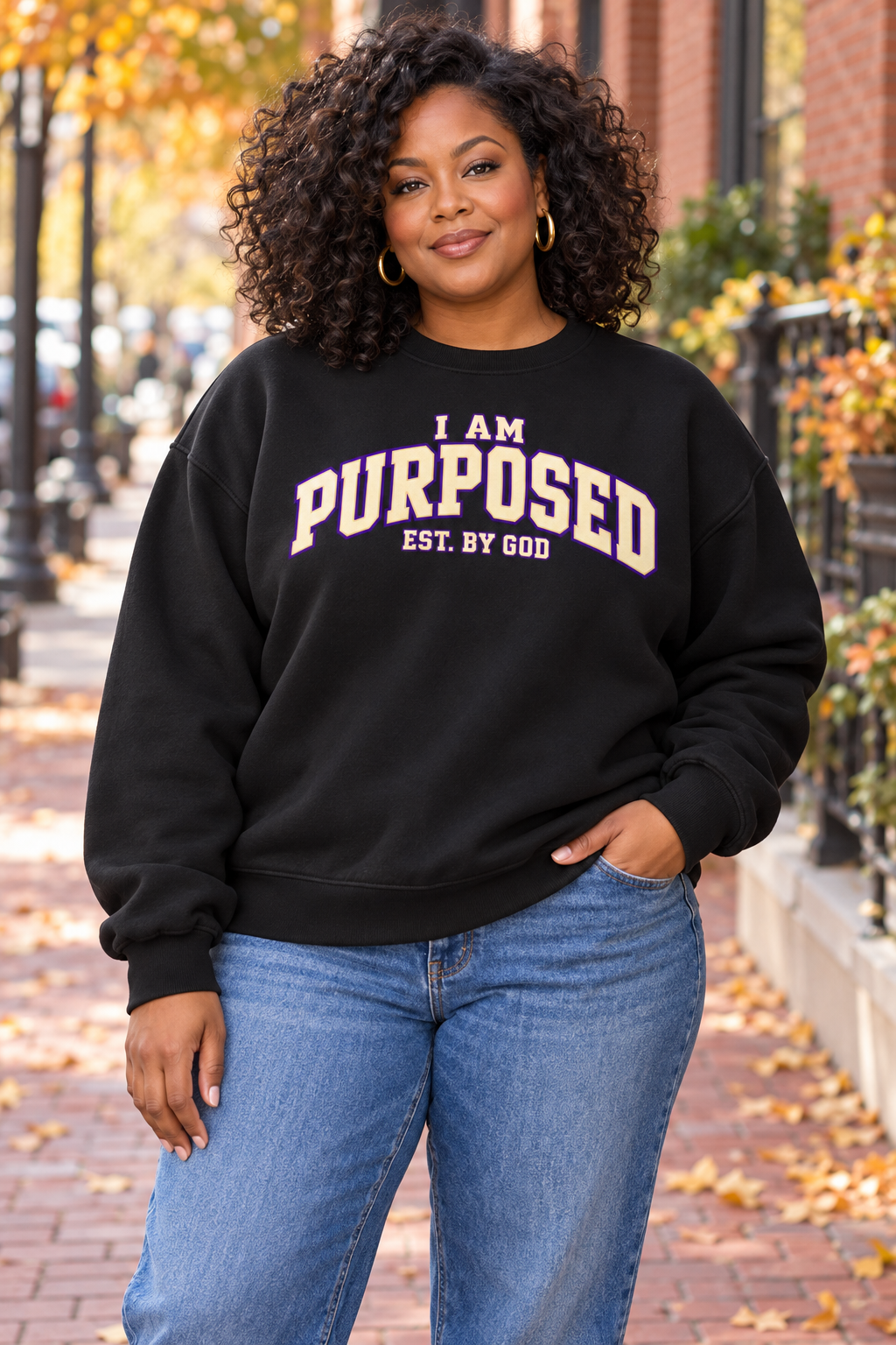 Lifestyle mockup of a woman wearing the black oversized I AM PURPOSED collegiate sweatshirt with EST. BY GOD beneath.
